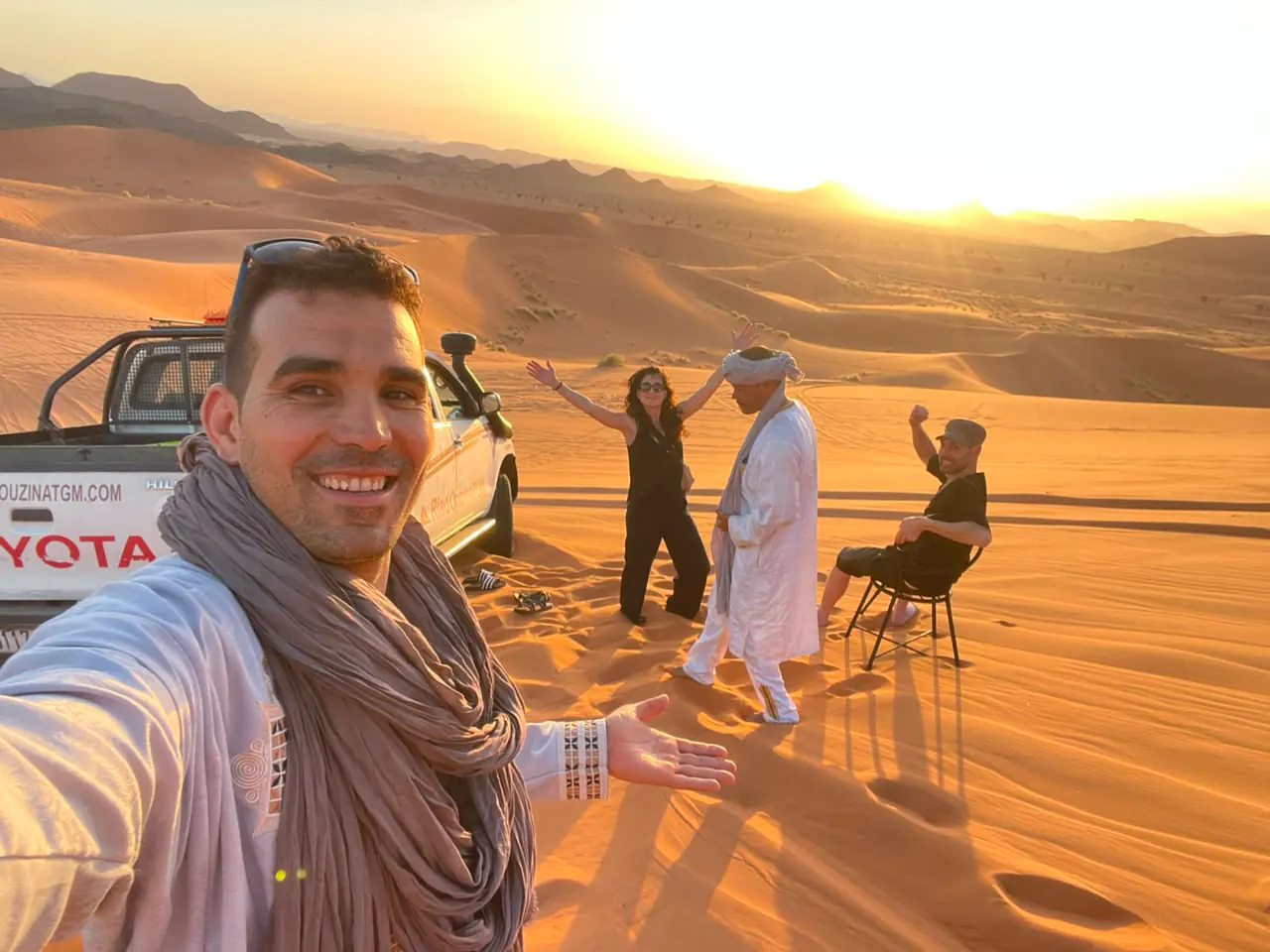 Guida che si scatta un selfie con i viaggiatori sulle dune al tramonto