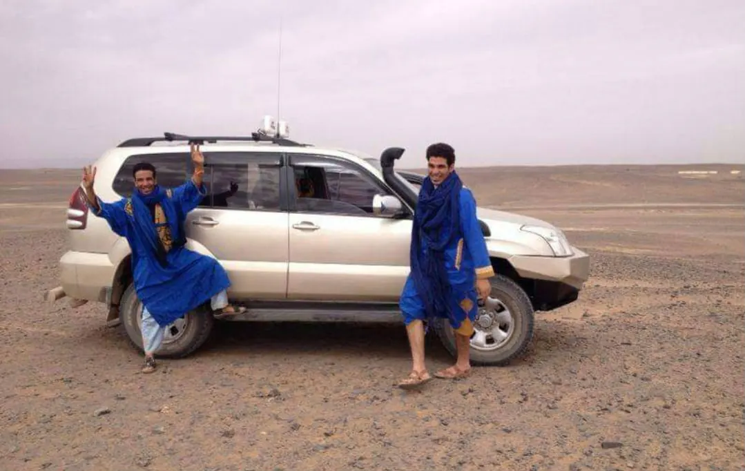 Due guide in abiti tradizionali blu accanto a un fuoristrada nel deserto