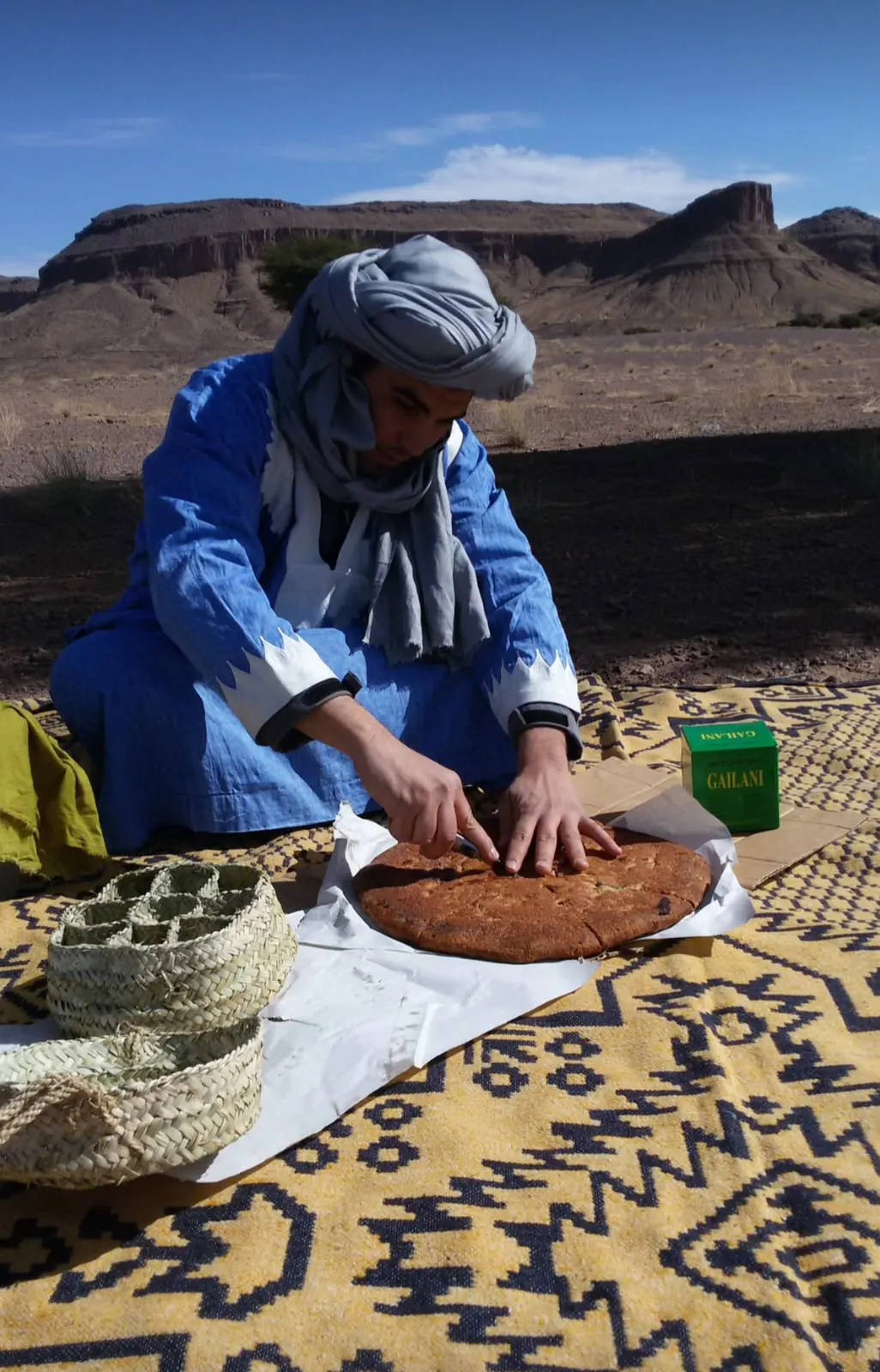 Guida berbera che taglia una madfouna, la pizza berbera, su un tappeto nel deserto