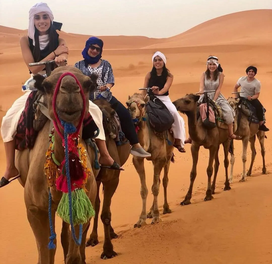 Gruppo di viaggiatori con il turbante durante un giro in cammello tra le dune