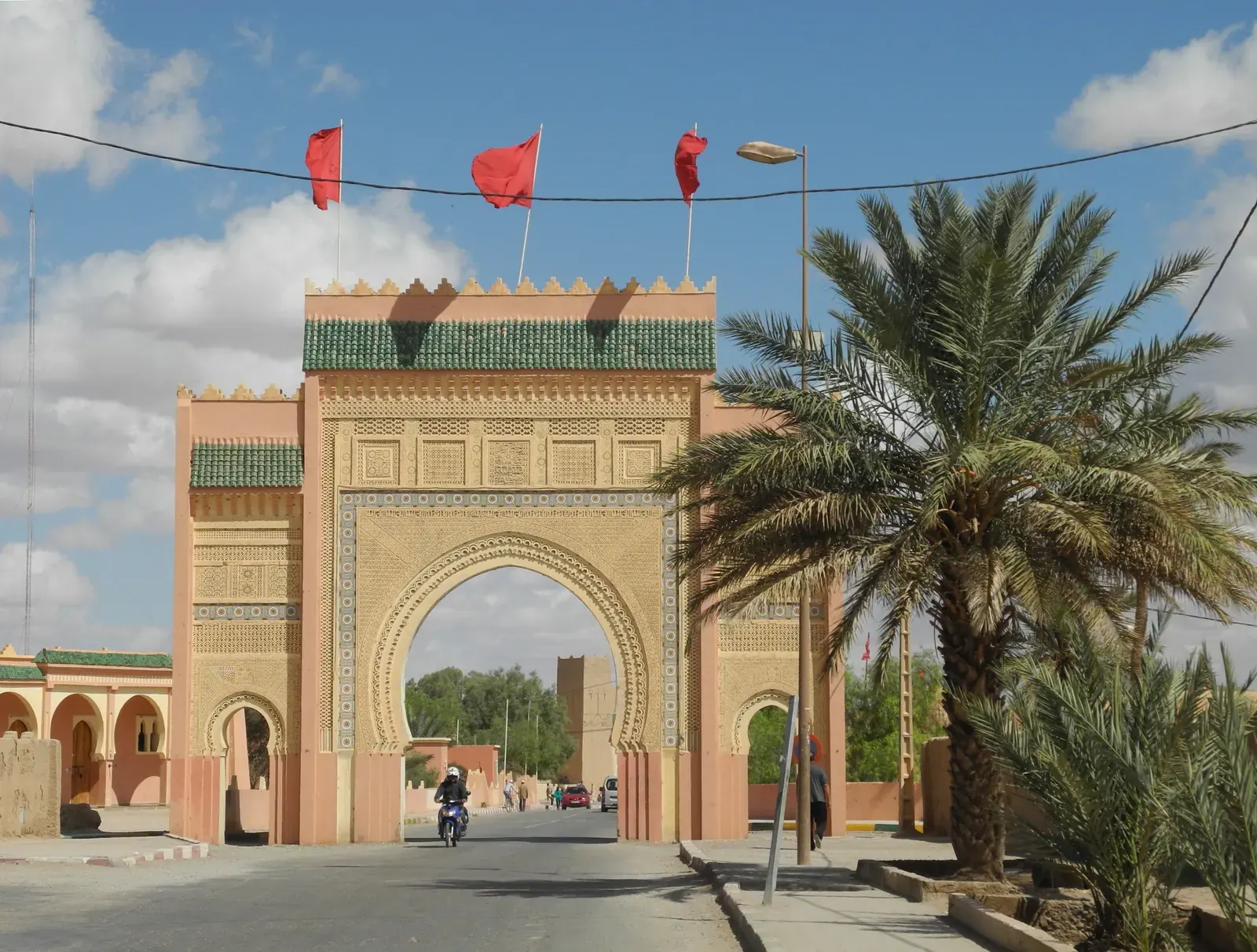 La porta monumentale d'ingresso a Rissani, con palme e bandiere marocchine