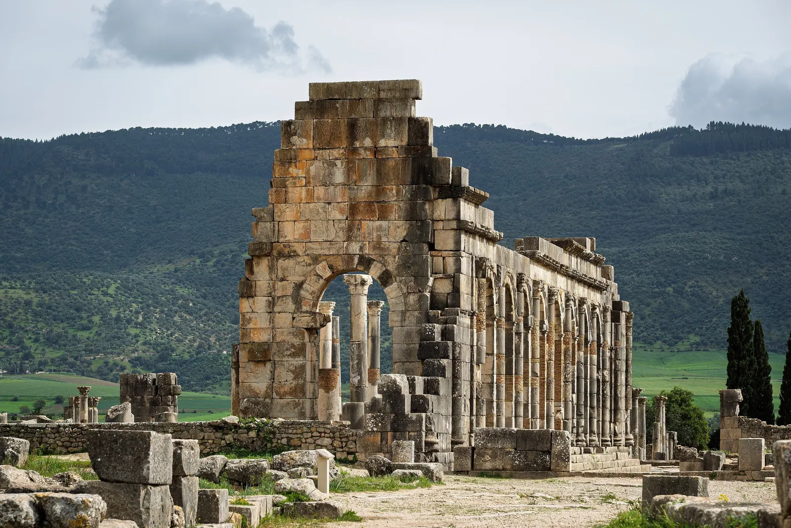 Colonne e archi della basilica romana di Volubilis, con verdi colline alle spalle